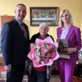Na fotografii jubilatka, wójt oraz zastępca kierownika USC. Jubilatka pozuje z kwiatami.