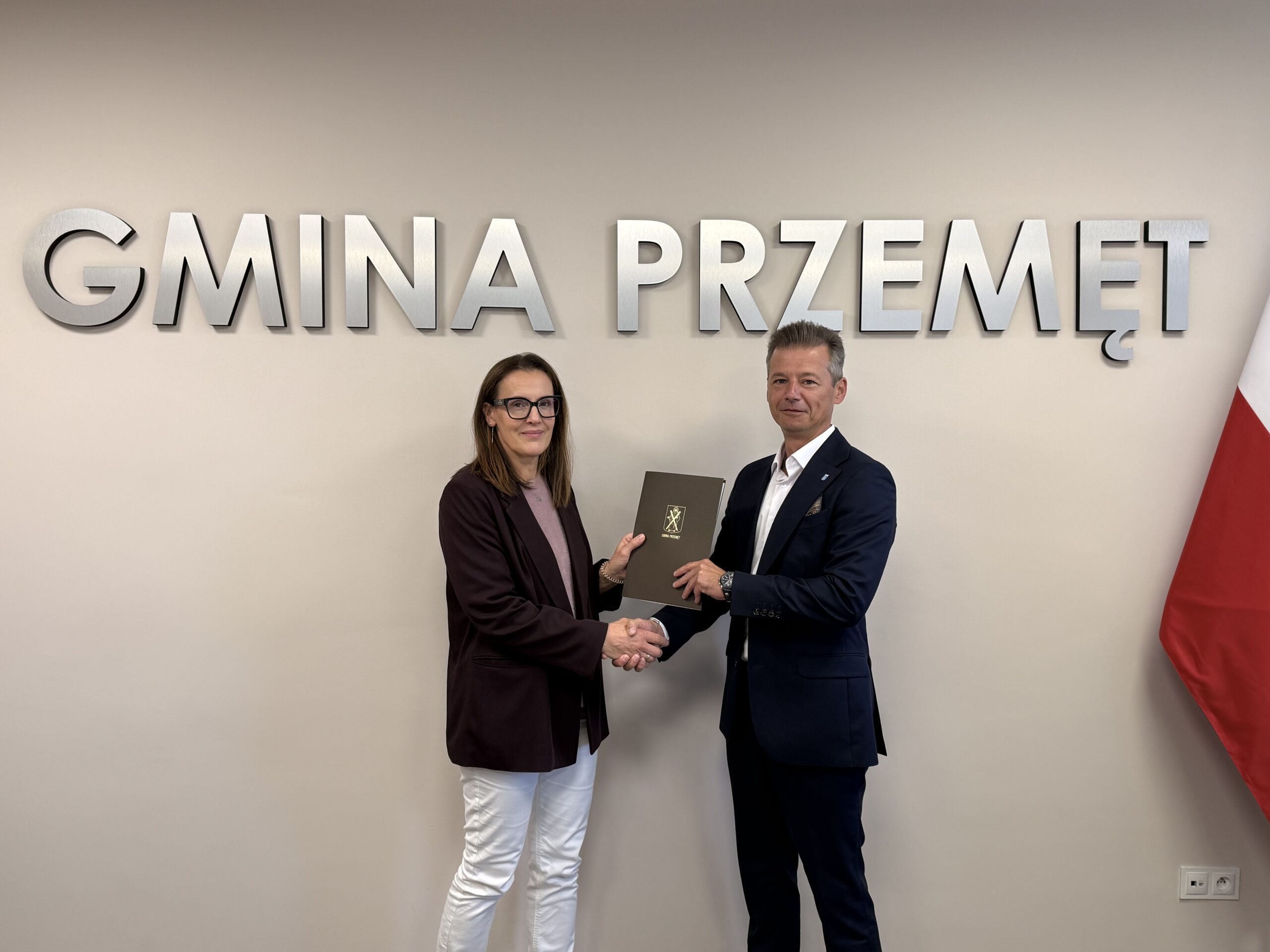 Na fotografii widoczny jest zastępca wójta, który podaje dłoń wykonawcy i przekazuje mu umowę. W tle srebrny napis Gmina Przemęt.